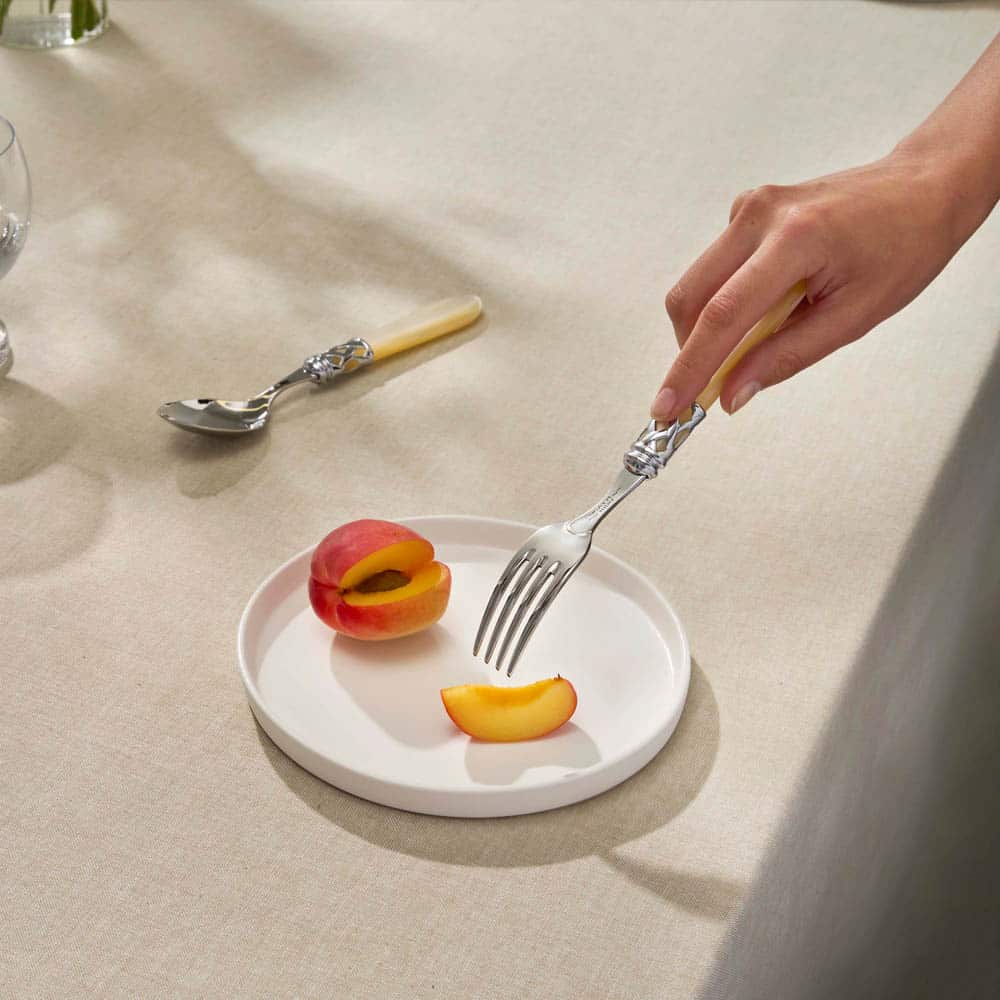 Cubertería con mango color hueso y detalle en plata en uso sobre plato de postre – menaje de mesa en contexto real