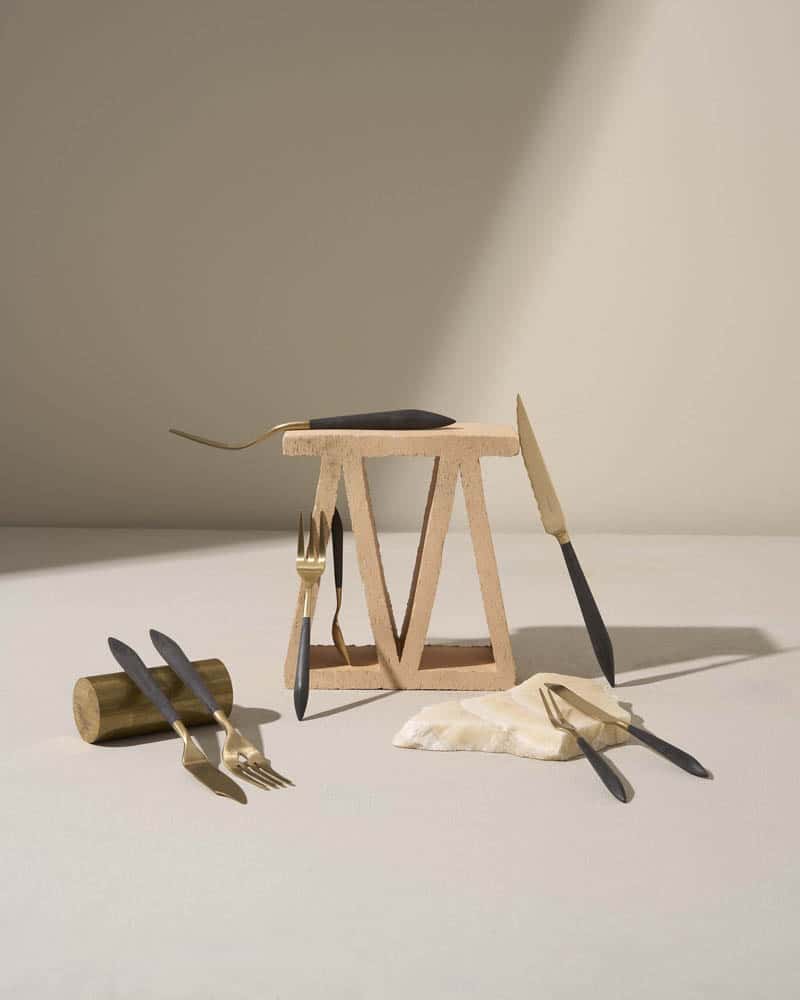 Cubertería de diseño en negro y dorado presentada sobre piedra y madera – menaje de autor para hostelería