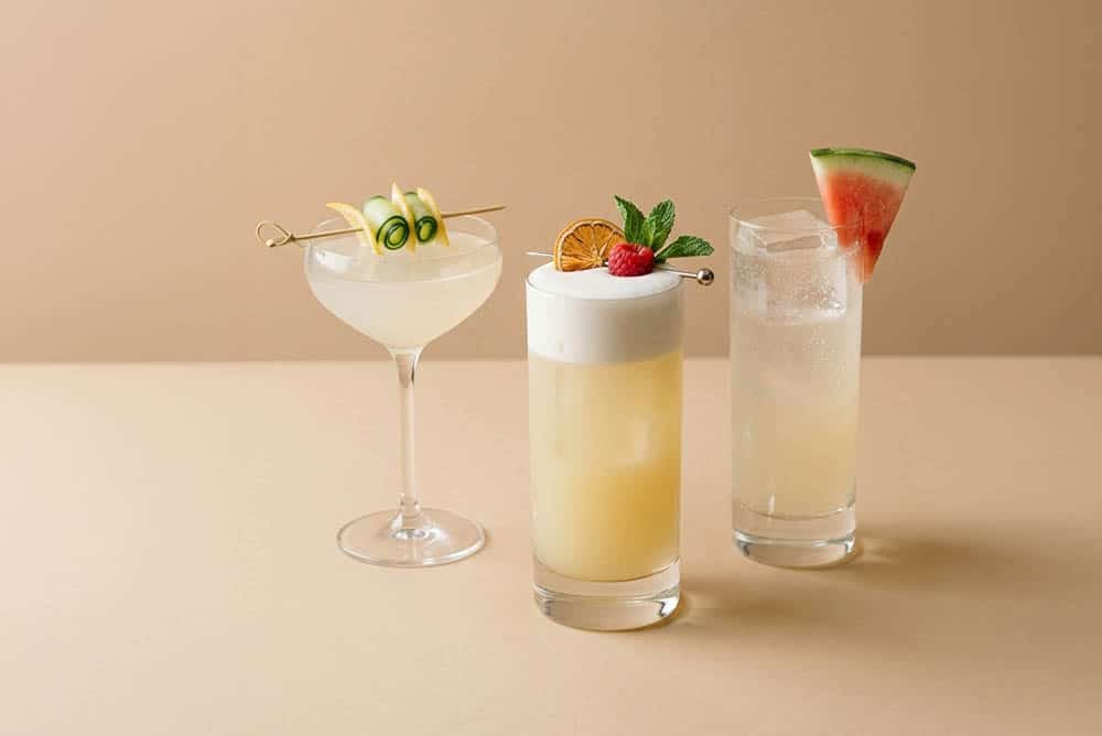Tres bebidas de coctelería con garnish de pepino y cítrico, naranja deshidratada con frambuesa y menta, y sandía