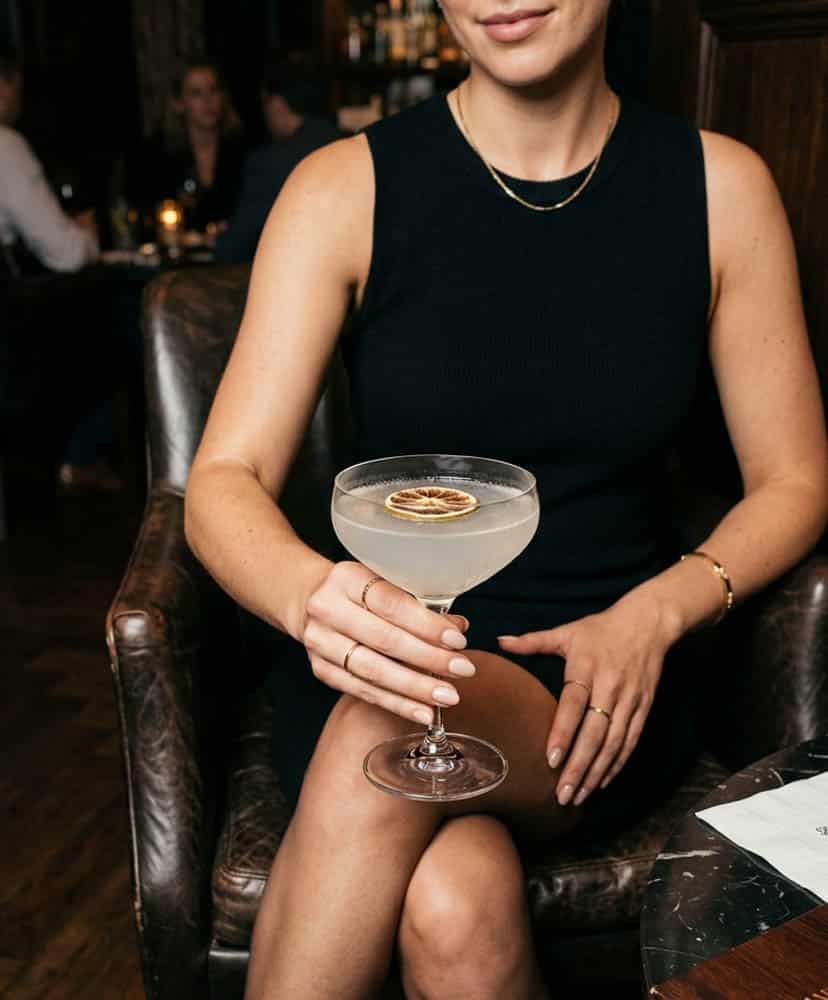 Copa coupe de cristal con un cóctel y rodaja de cítrico deshidratado como garnish en un bar de ambiente íntimo